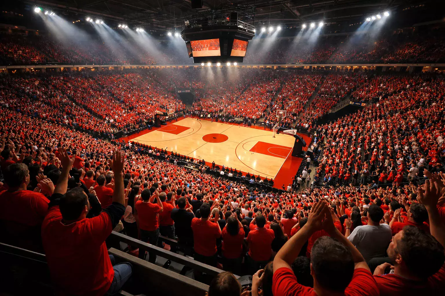 Mano de un aficionado sosteniendo un móvil con un partido de baloncesto de fondo en la arena