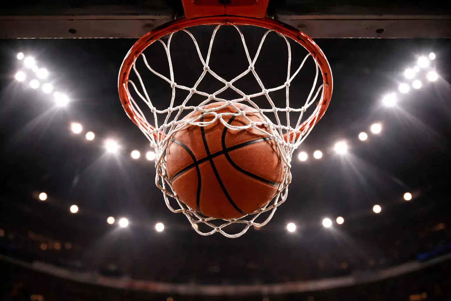 Balón de baloncesto entrando en la red de la canasta visto desde abajo en un pabellón